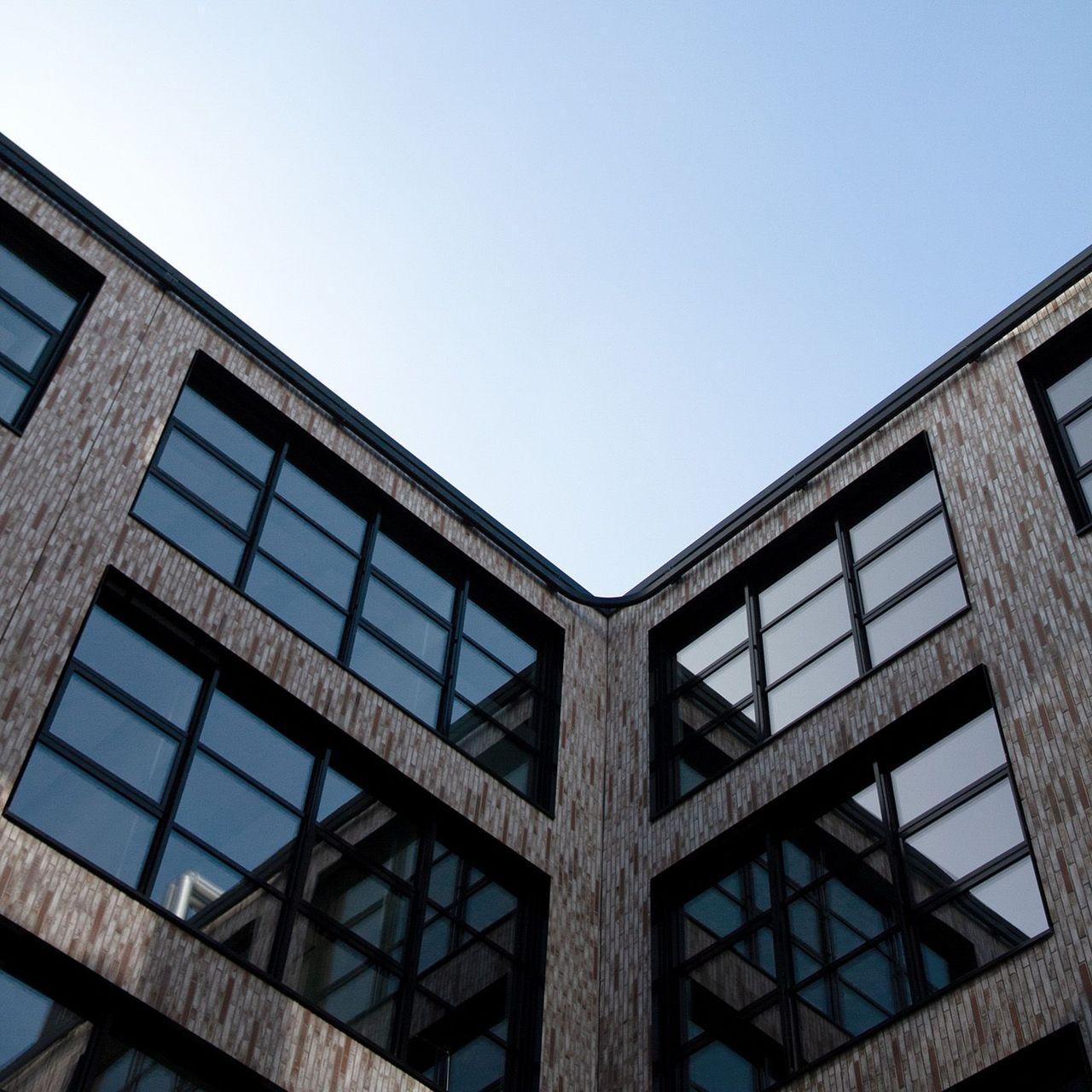 Ansicht des Innenhofs des Gebäudekomplexes Neue Siederei aus einer niedrigen Perspektive, die den blauen Himmel und die großen Fenster des modernen Backsteinbaus zeigt.