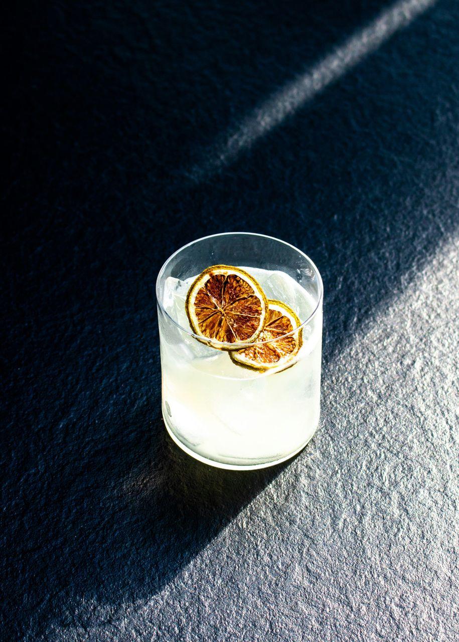 Nahaufnahme eines erfrischenden Cocktails in einem Glas mit Eis und getrockneten Orangenscheiben, serviert bei einem Afterwork-Event auf der Dachterrasse.