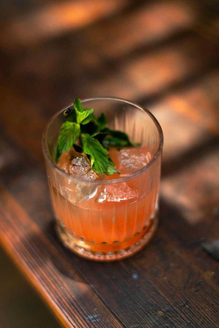 Ein Cocktail in einem Glas mit Eiswürfeln und Minzblättern, auf einem Holztisch serviert, passend zu einem Afterwork-Cocktailabend auf der Dachterrasse.